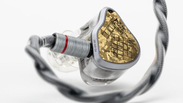 Nahaufnahme eines hochwertigen In-Ear-Kopfhörers mit goldfarbener Abdeckung und geflochtenem Kabel.