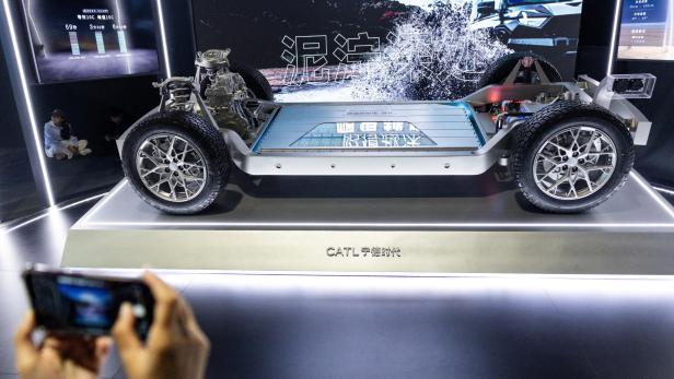 Ein elektrisches Fahrzeug-Chassis mit sichtbarem Batteriepaket und Reifen wird auf einer Messe ausgestellt.