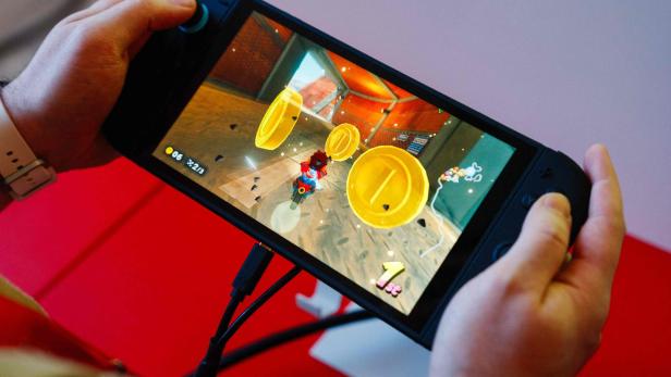 Hände halten eine Nintendo Switch, auf der ein Rennspiel mit Münzen und einer „1st“-Platzierung angezeigt wird.