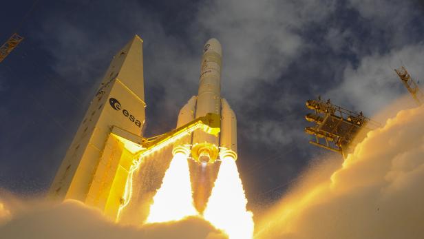 Eine Ariane-Rakete der ESA startet mit leuchtenden Feststoffboostern und erzeugt dichte Rauch- und Feuersäulen am Boden.