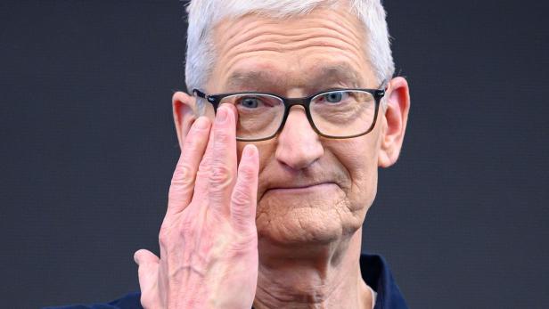 Ein älterer Mann mit Brille hebt die Hand an sein Gesicht und blickt nach vorne.