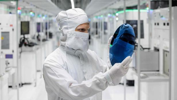 Eine Person im Reinraumanzug hält eine Siliziumscheibe in einer modernen Hightech-Fertigungsanlage.