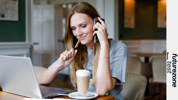 Eine Frau sitzt vor dem Notebook und telefoniert am Smartphone.