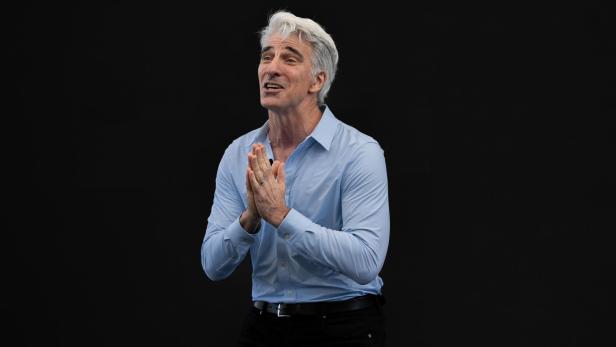 Craig Federighi steht vor einem schwarzen Hintergrund und hält seine Hände dankbar vor der Brust zusammen.