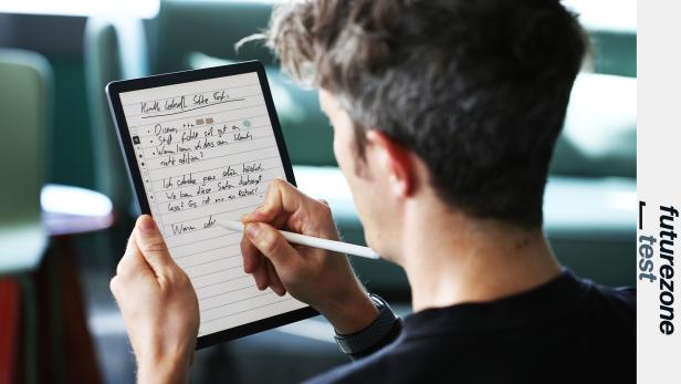 Eine Person schreibt mit einem Stift handschriftliche Notizen auf einem Tablet mit liniertem Bildschirm.