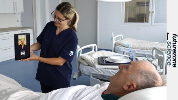 Pflegekraft zeigt per Tablet eine Video-Sprechstunde einem Patienten im Krankenhauszimmer.