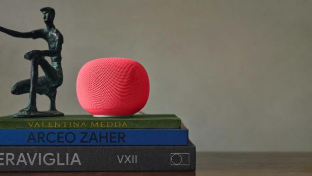 Eine rote Smart-Speaker-Kugel neben einer kleinen Skulptur auf gestapelten Büchern.