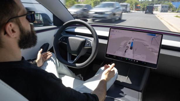Mann sitzt in einem Tesla und blickt auf die Straße, während das Autopilot-Display die Fahrt anzeigt.