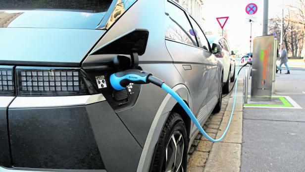 Graues Elektroauto lädt an einer Straßensäule am Bordstein.