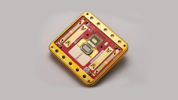 Microsofts Quantenchip Majorana 1 in einem goldenen Gehäuse auf grauem Hintergrund.