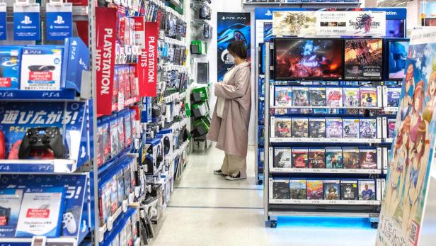 Kundin in einem PlayStation-Regalgang prüft Spiele und Zubehör im Elektronikmarkt.