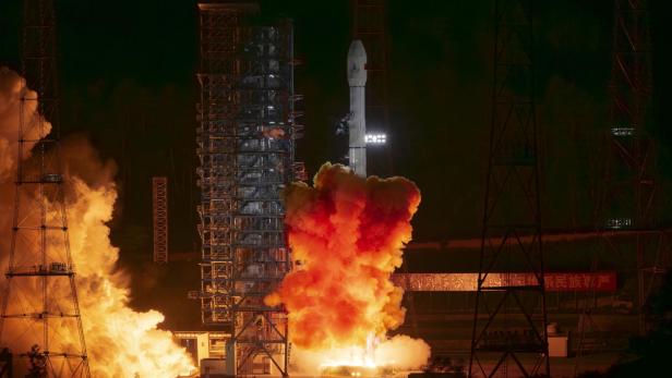 Rakete startet nachts auf der Startrampe, umgeben von grellen Flammen und dichtem Rauch.
