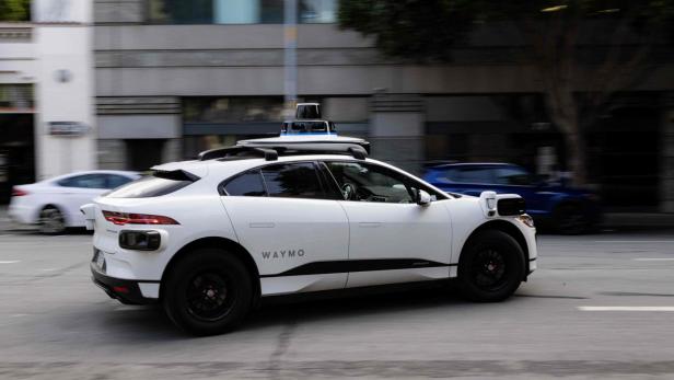 Weißes Waymo-Selbstfahrauto fährt durch eine Stadtstraße.