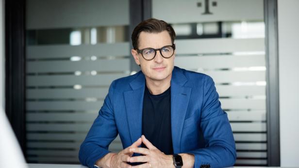 Thomas Kicker sitzt im Büro vor einer Glastür mit Telekom-Logo.