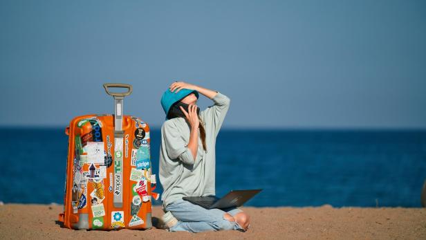 Frau mit Koffer und Handy am Strand
