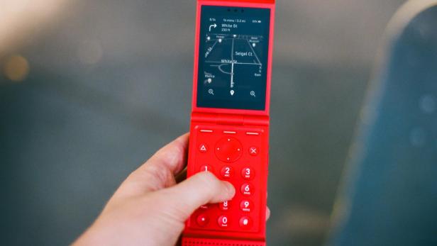 Eine Hand hält ein aufgeklapptes, knallrotes Flip Light mit Schwarz-Weiß-Display