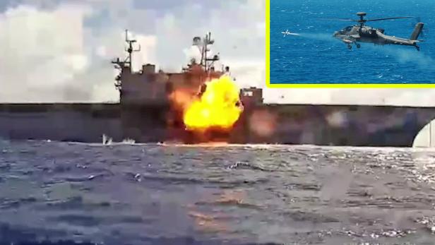 Eine Explosion ist mittig auf einem Schiff zu sehen. Rechts oben feuert ein Kampfhubschrauber eine Rakete ab.