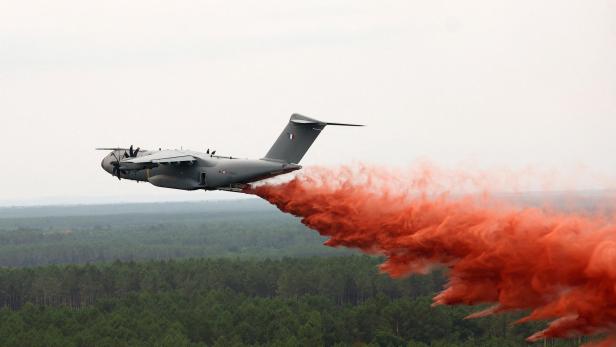 Graues Löschflugzeug wirft rote Brandbekämpfungsflüssigkeit über einem Wald ab.