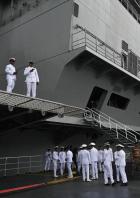 Eine Gruppe von Marineangehörigen steht vor einem grauen Kriegsschiff.