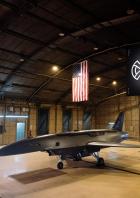 Ein YFQ-44A-Flugzeug steht in einem Hangar mit einer US-Flagge und einem Banner.