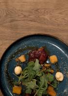 Ein Teller mit einem Gericht aus Fleisch, Gemüse und Soße auf einem Holztisch.