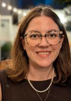 Eine lächelnde Frau mit Brille und Perlenkette in einem Restaurant.