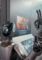 Der Küchenroboter Robbyant steht auf einer Messe neben einem Bildschirm mit Rezepten.