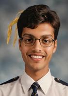 Ein lächelnder junger Mann mit Brille und Uniform vor einem neutralen Hintergrund.