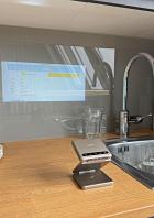 Eine Aurzen ZIP Küchenwaage steht vor einer Küchenspüle, auf der ein Rezept projiziert wird.