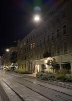 Eine Straßenbahnhaltestelle in einer belebten Straße bei Nacht.