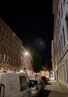 Eine nächtliche Straßenszene mit geparkten Lieferwagen und Wohnhäusern.