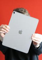 Person hält ein silbernes iPad Air 13 vor rotem Hintergrund in beiden Händen.
