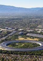 Luftaufnahme des kreisförmigen Apple Park Campus in Cupertino mit umliegenden Wohngebieten und Bergen im Hintergrund.