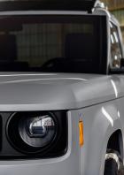 Ein grauer, kantiger Slate-E-Pick-up mit kurzer Ladefläche steht vor einer Wellblechwand.