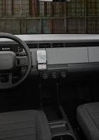 Ein grauer, kantiger Slate-E-Pick-up mit kurzer Ladefläche steht vor einer Wellblechwand.