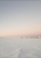 Die Amundsen-Scott-Südpolstation liegt in einer weiten, schneebedeckten Eislandschaft unter einem pastellfarbenen Dämmerungshimmel.
