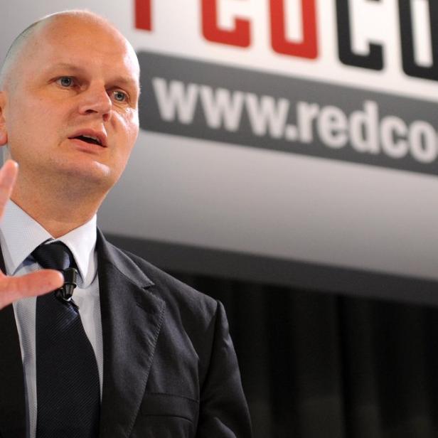 Ein Mann im Anzug gestikuliert vor einem Banner mit der Aufschrift „redcoon.de“.