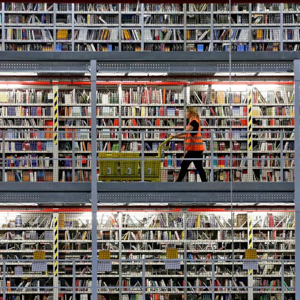 Eine Frau schiebt einen Wagen mit einer Kiste in einem Lagerhaus voller Bücherregale.