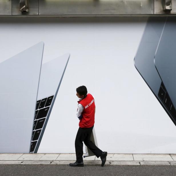 Ein Mann geht an einer Wand mit einer großen Apple-Laptop-Werbung vorbei.