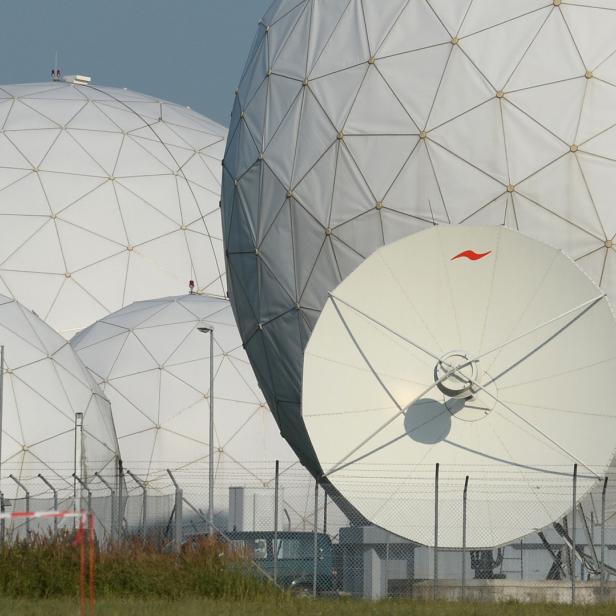 Mehrere weiße Radarkuppeln und eine Satellitenschüssel hinter einem Zaun.