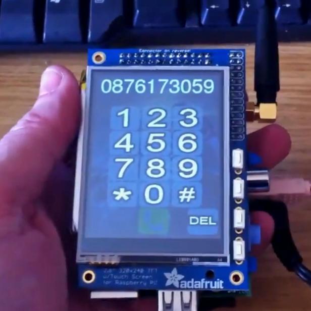 Eine Hand hält ein Gerät mit Touchscreen, das ein Tastenfeld und eine eingegebene Telefonnummer zeigt.