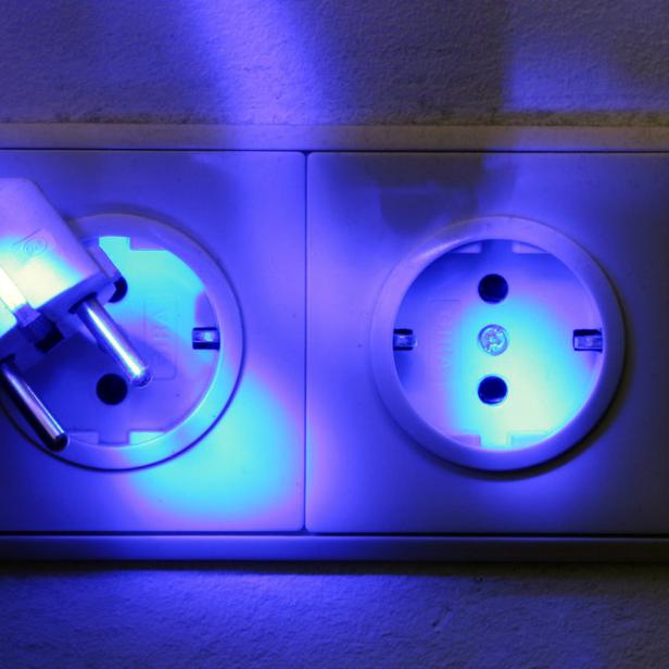 Ein Stecker steckt in einer Steckdose, die bläulich beleuchtet ist.