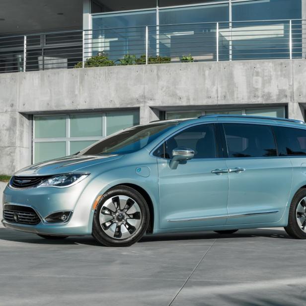 Ein hellblauer Chrysler Pacifica Hybrid vor einem modernen Haus.