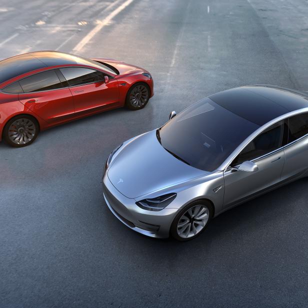 Ein roter und ein silberner Tesla Model 3 stehen auf einem Parkplatz.
