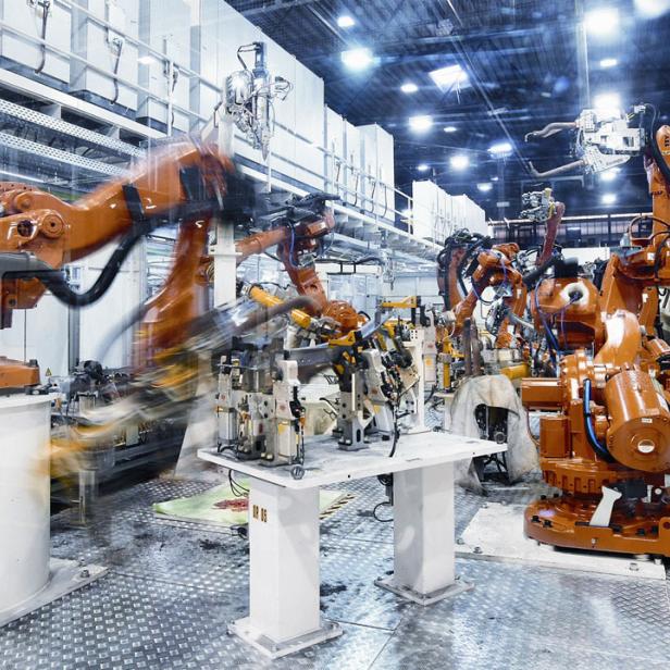 Mehrere orangefarbene Industrieroboter arbeiten in einer Fabrikhalle.