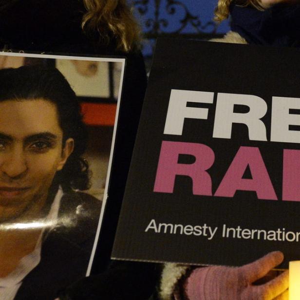 Eine Person hält ein Foto von Raif Badawi und ein Schild mit der Aufschrift „Free Raif“ von Amnesty International.