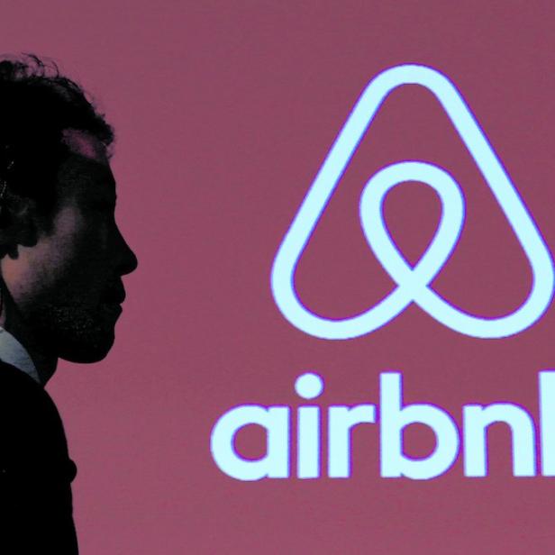 Ein Mann im Anzug steht vor dem Airbnb-Logo.