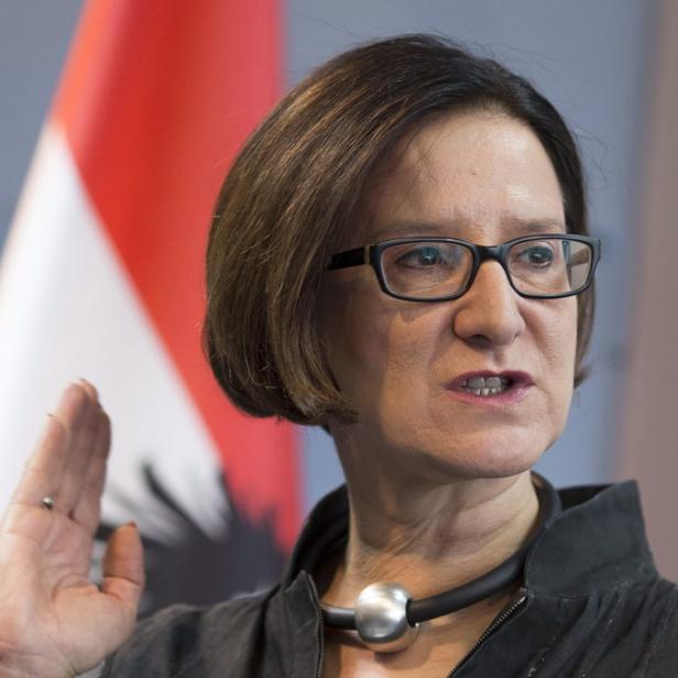 Eine Frau mit Brille hält ihre Hand vor einer österreichischen Flagge hoch.