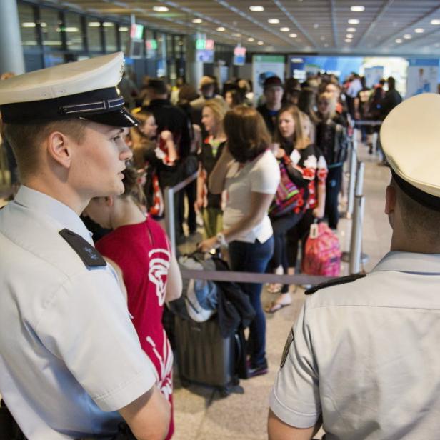 Zwei Polizisten beobachten eine lange Schlange von Reisenden am Flughafen.