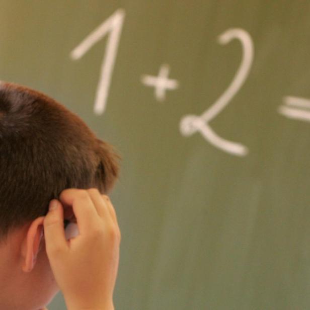 Ein Junge steht vor einer Tafel mit der Frage „1+2=?“.